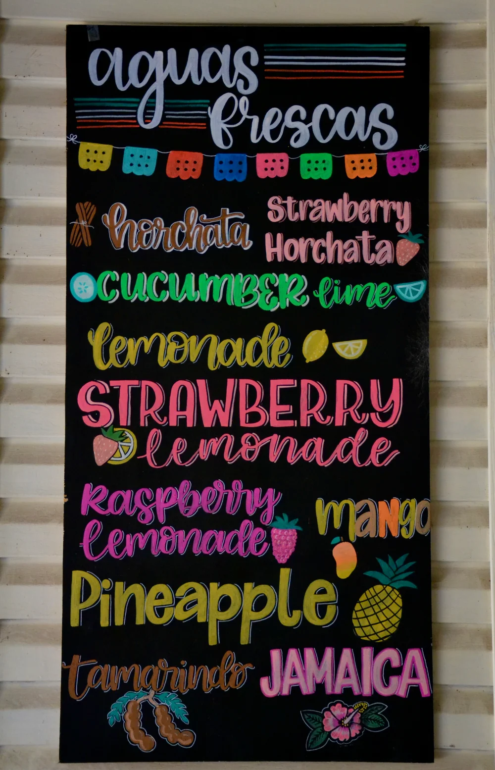 A hand-lettered aguas frescas board listing horchata and fruit drink flavors