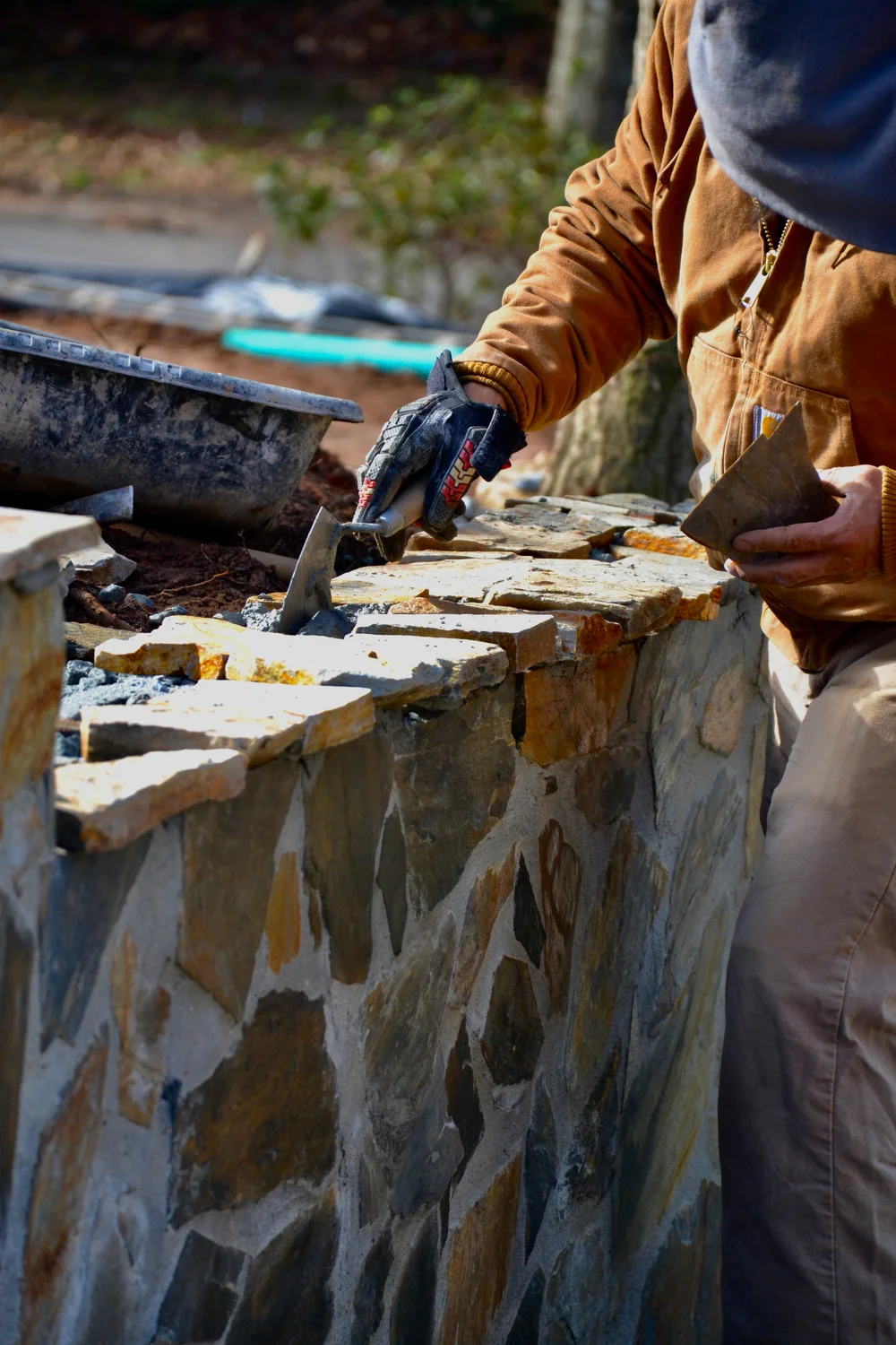 A Dos Guys craftsperson shaping a stone retaining wall by hand