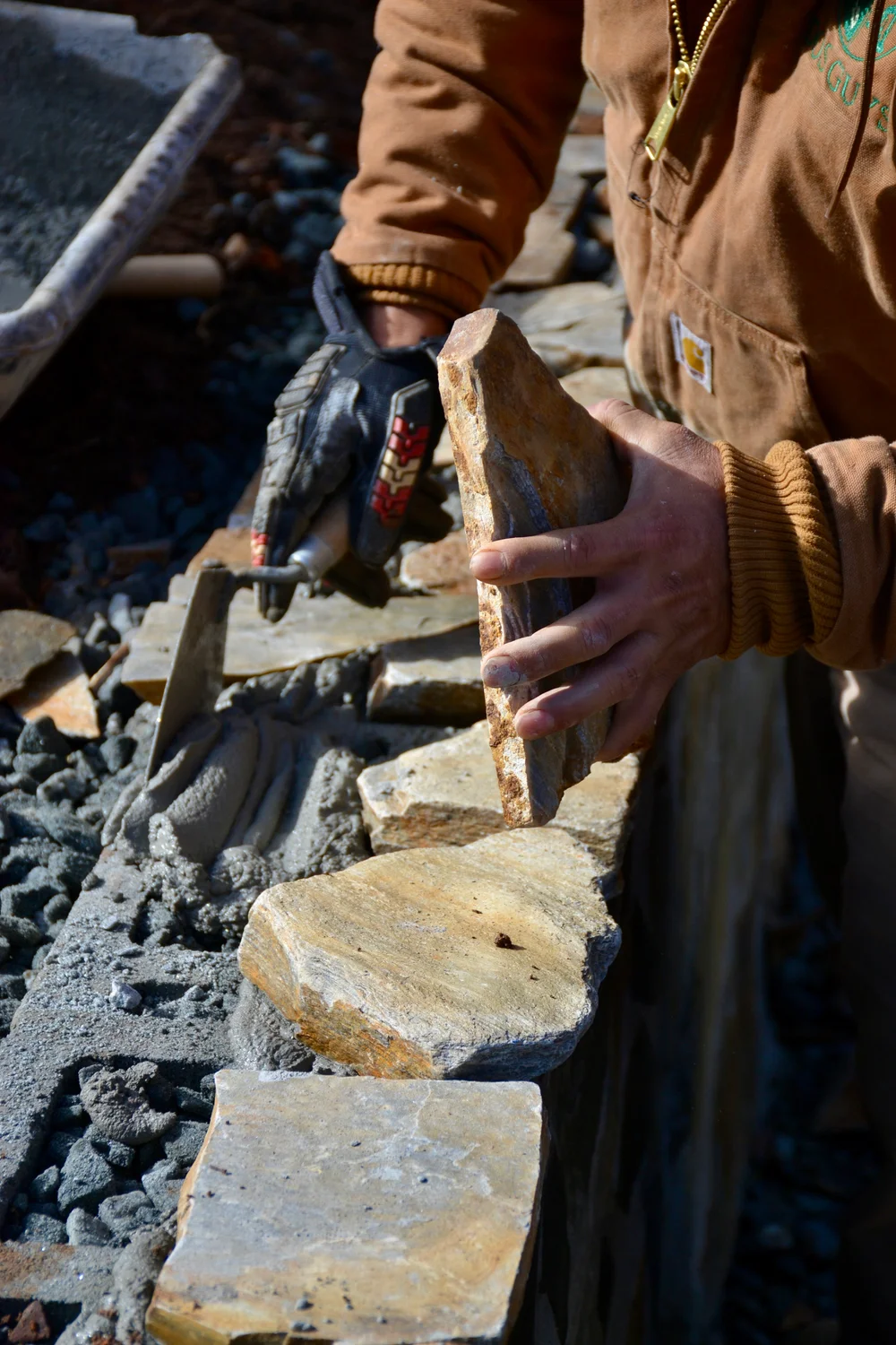 Hands positioning a stone above fresh mortar on a retaining wall
